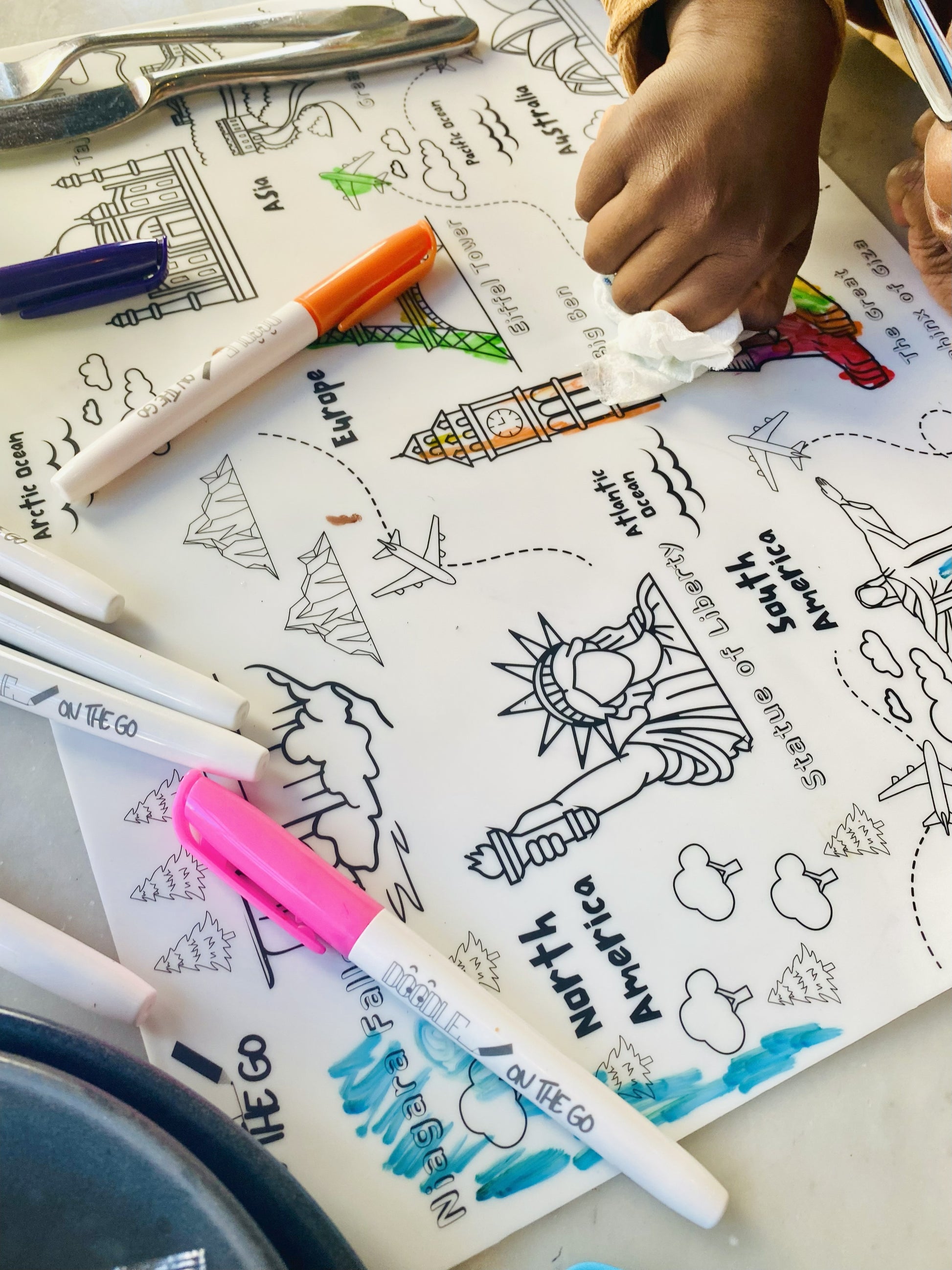 Child’s hand cleaning reusable Animal Footprint Tracker mat at a restaurant table